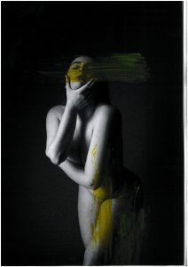 A black and white photograph of a nude female which has been physically manipulated with yellow paint smeared across it.
