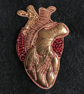 An anatomical brooch of a human head created using goldwork and beading