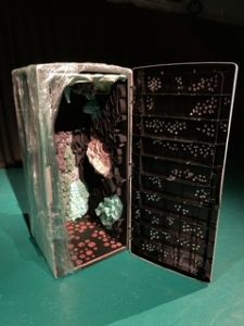 Large rectangular container with its door open. Inside there are different materials creating circular patterns and ruffled textures. The outside of the box is covered with translucent plastic.  