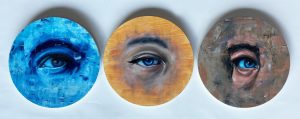 Three circular paintings of close ups of eyes. 
One is only in shades of blue and the others are painted naturally. 