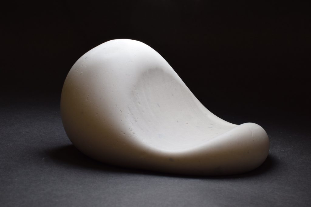 A simple white curved sculpture on a black background.