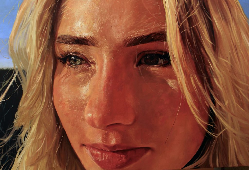 A close-up realistic portrait of a young woman's face. The sun is bright on her face. She has blue eyes and blonde hair. 