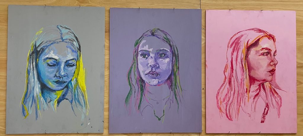 Three portrait painting of a girl; one in blue and yellow paint she is glancing down, another in purple and green paint she is facing forward but looking to the side, the last is in red and yellow paint she is looking to the right. 